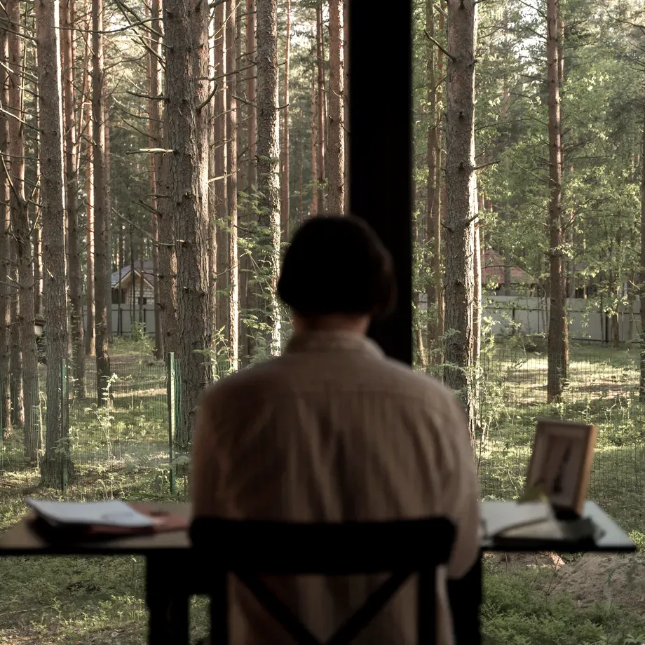 Person seen from behind working at a desk in front of a panoramic window overlooking a forest
