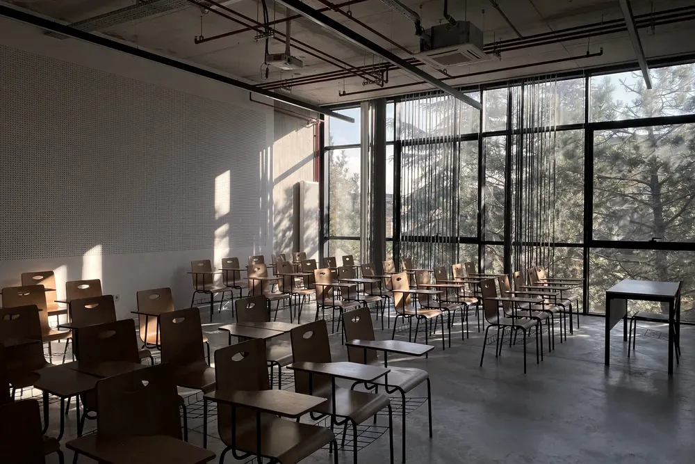 Empty classroom with wooden chair-desks and a full-height window onto trees