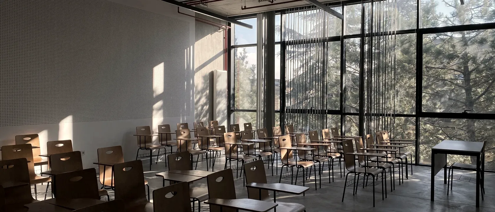 Empty classroom with wooden chair-desks and a full-height window onto trees