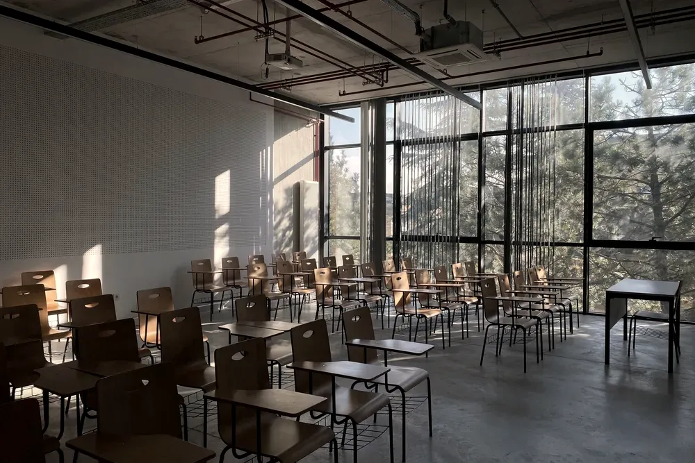 Empty classroom with wooden chair-desks and a full-height window onto trees