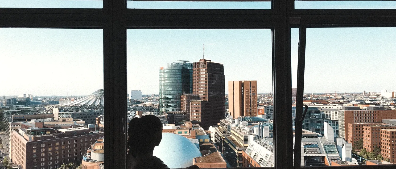 Silhouette of a person sitting at a floor-to-ceiling window with a view over Potsdamer Platz in Berlin